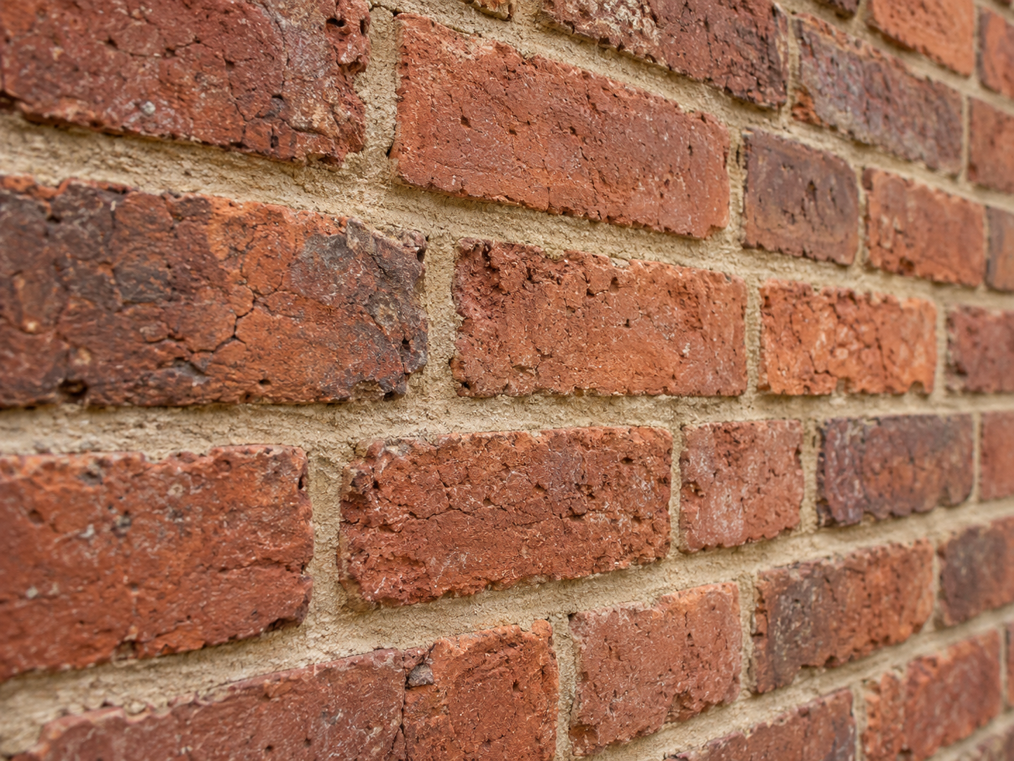 Close view of porous red brick with recessed, warm sandy lime mortar joints that sit softer than the surrounding masonry.