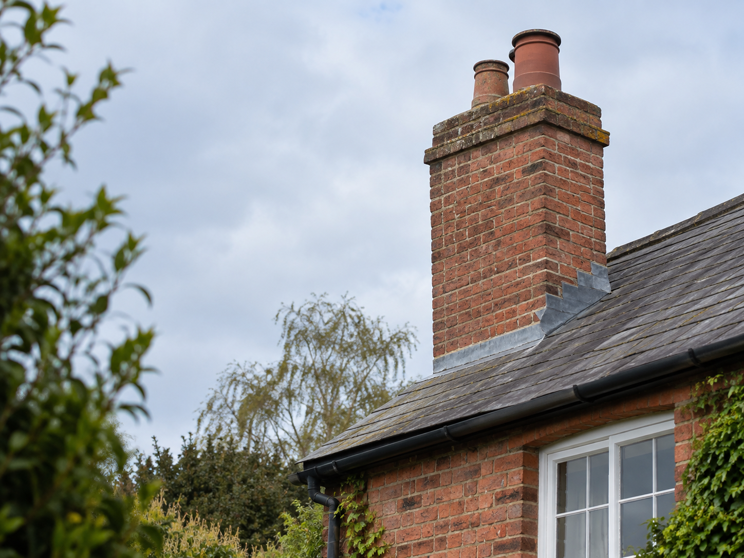Traditional red-brick chimney stack with weathered joints and lead flashing viewed safely from ground level above a slate roof.